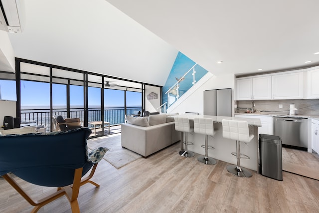 living room featuring a wall unit AC, sink, a water view, and light hardwood / wood-style floors