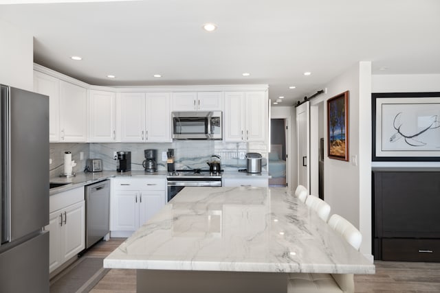 kitchen with stainless steel appliances, a barn door, white cabinets, hardwood / wood-style floors, and a center island