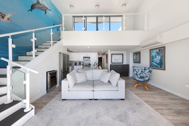 living room with an AC wall unit, beverage cooler, light hardwood / wood-style floors, and a high ceiling