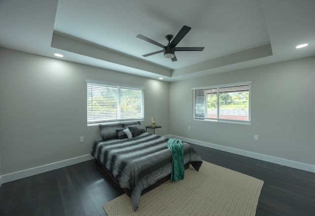 bedroom featuring a tray ceiling, multiple windows, ceiling fan, and dark wood-type flooring