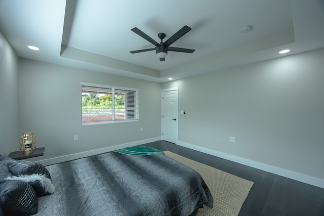 bedroom featuring ceiling fan, dark hardwood / wood-style flooring, and a tray ceiling