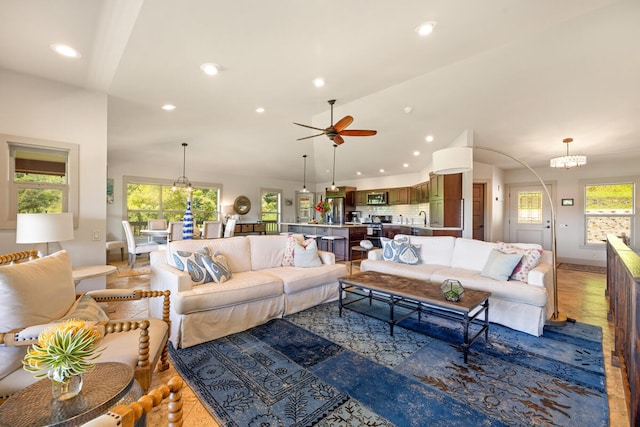 living room with ceiling fan with notable chandelier, a healthy amount of sunlight, wood-type flooring, and vaulted ceiling