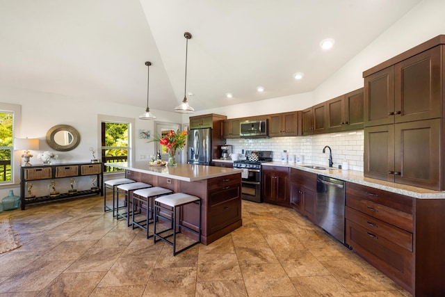 kitchen with a breakfast bar, a center island, hanging light fixtures, vaulted ceiling, and stainless steel appliances