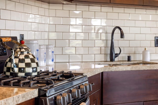 interior details with gas stove, decorative backsplash, sink, and light stone counters