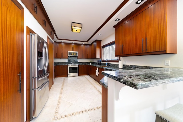 kitchen with dark stone counters, sink, appliances with stainless steel finishes, a kitchen bar, and kitchen peninsula