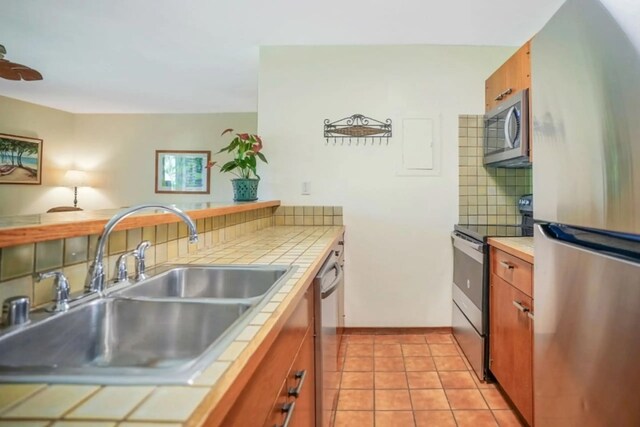 kitchen featuring appliances with stainless steel finishes, tasteful backsplash, sink, light tile patterned floors, and tile counters