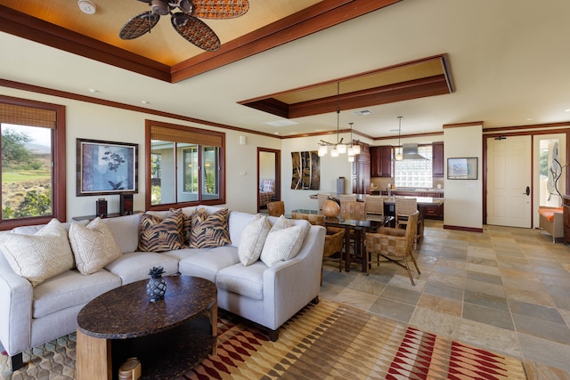 living room featuring ceiling fan with notable chandelier, a tray ceiling, plenty of natural light, and crown molding