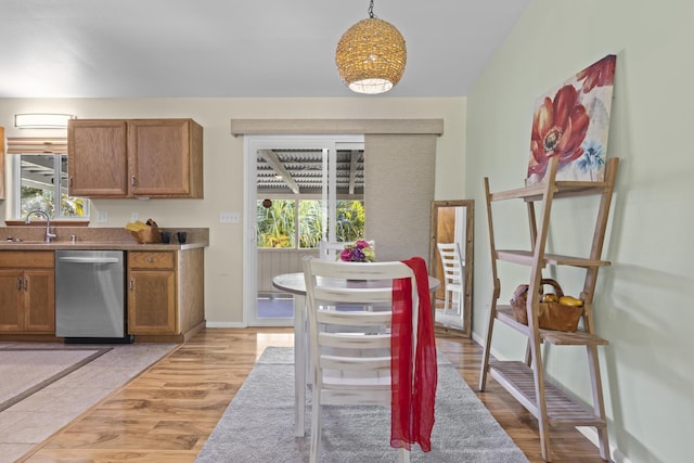 kitchen featuring stainless steel dishwasher, light hardwood / wood-style flooring, hanging light fixtures, and plenty of natural light