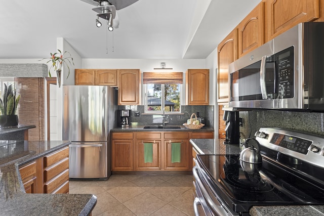 kitchen featuring sink, decorative backsplash, dark stone countertops, light tile patterned floors, and stainless steel appliances