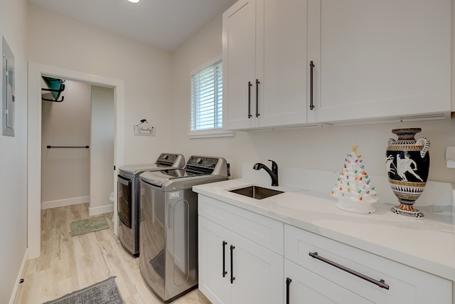 clothes washing area with cabinets, light hardwood / wood-style floors, washing machine and dryer, and sink