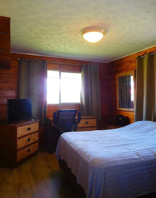 bedroom with wood walls, dark wood-type flooring, and a textured ceiling