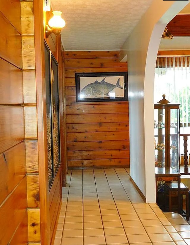 hallway with a textured ceiling, tile patterned floors, and wood walls