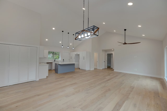 interior space with white cabinetry, hanging light fixtures, high vaulted ceiling, a kitchen island, and light wood-type flooring