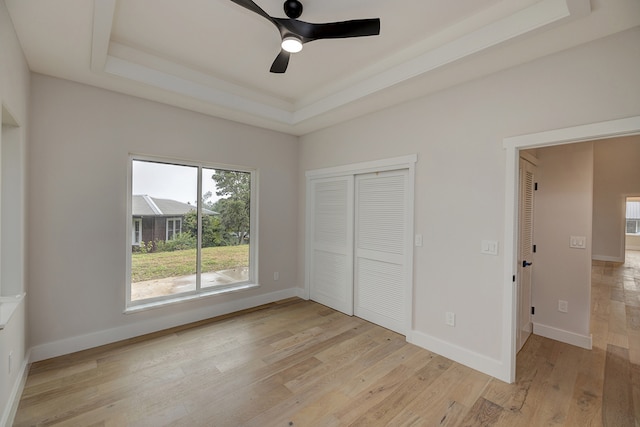 unfurnished bedroom featuring a closet, light hardwood / wood-style floors, a raised ceiling, and ceiling fan