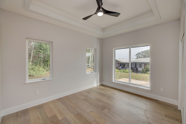 empty room with ceiling fan, light wood-type flooring, and a tray ceiling