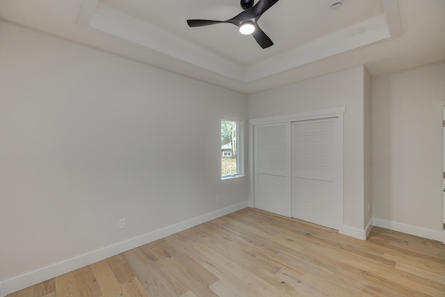 unfurnished bedroom featuring a closet, light hardwood / wood-style floors, a raised ceiling, and ceiling fan