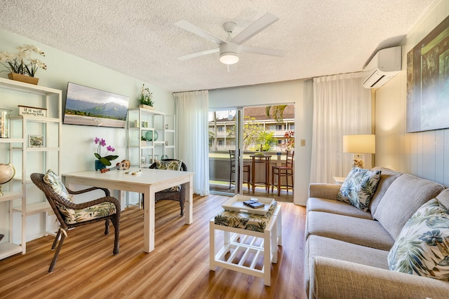 living room featuring a textured ceiling, ceiling fan, a wall mounted air conditioner, and light wood-type flooring