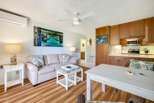 living room featuring an AC wall unit, ceiling fan, a textured ceiling, and light wood-type flooring