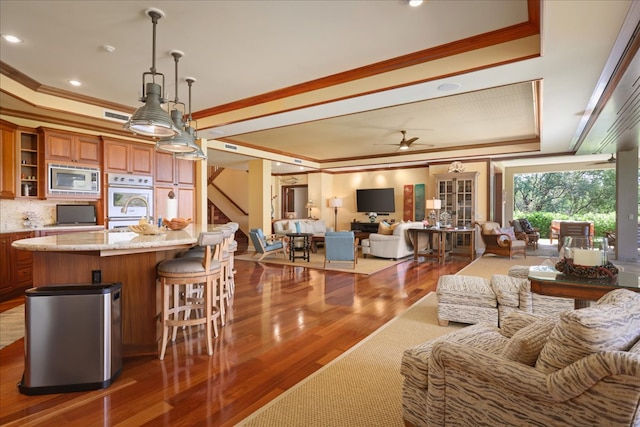 kitchen featuring stainless steel microwave, dark wood-type flooring, a raised ceiling, decorative light fixtures, and ornamental molding