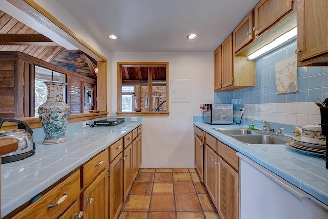 kitchen featuring tile countertops, backsplash, a sink, and brown cabinets