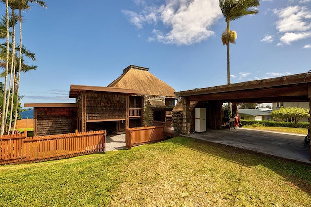 rear view of property with an attached carport, a lawn, driveway, and fence