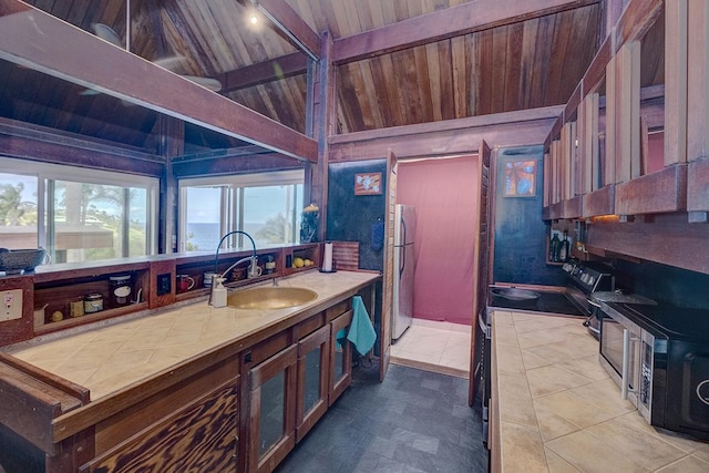 kitchen featuring tile countertops, lofted ceiling with beams, wooden ceiling, a sink, and freestanding refrigerator