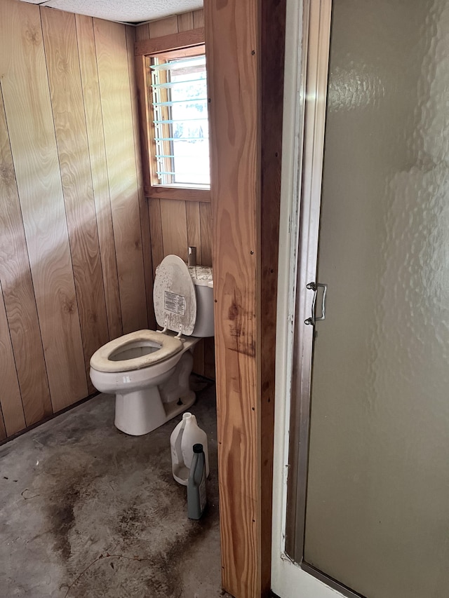 bathroom featuring a textured ceiling, toilet, walk in shower, and wooden walls