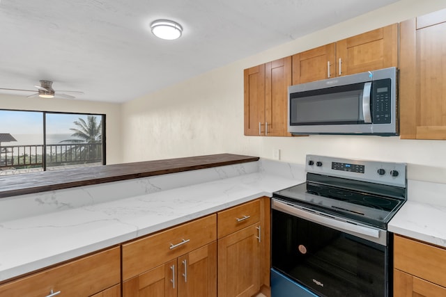 kitchen featuring ceiling fan, stainless steel appliances, and light stone counters