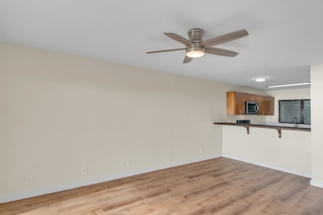 unfurnished living room featuring ceiling fan, light wood-type flooring, and sink