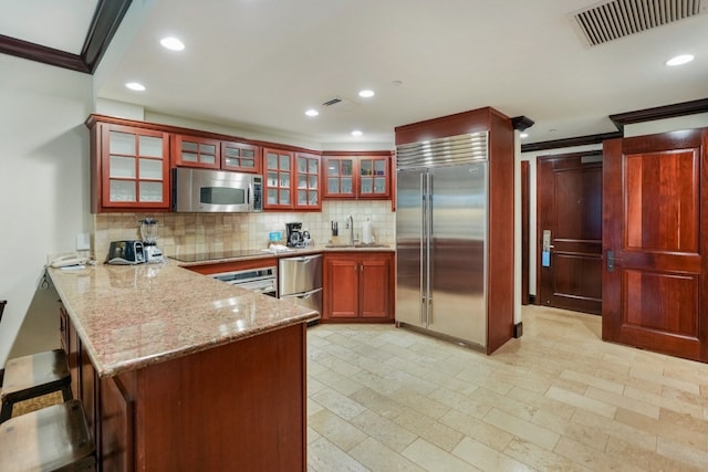 kitchen with crown molding, decorative backsplash, appliances with stainless steel finishes, light stone counters, and kitchen peninsula