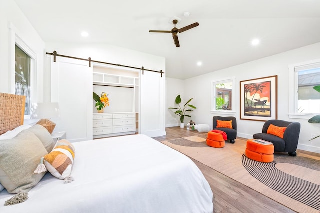 bedroom with light wood-type flooring, a barn door, vaulted ceiling, and ceiling fan