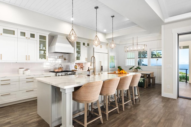 kitchen featuring hanging light fixtures, a spacious island, a kitchen bar, white cabinets, and custom exhaust hood