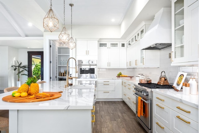 kitchen with a kitchen island with sink, white cabinets, custom range hood, and appliances with stainless steel finishes