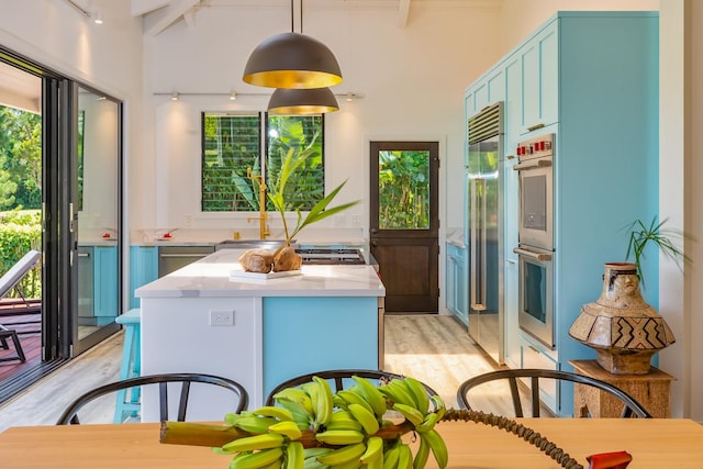 kitchen featuring rail lighting, vaulted ceiling with beams, blue cabinets, light hardwood / wood-style floors, and decorative light fixtures