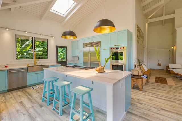 kitchen featuring high vaulted ceiling, a skylight, appliances with stainless steel finishes, beamed ceiling, and decorative light fixtures