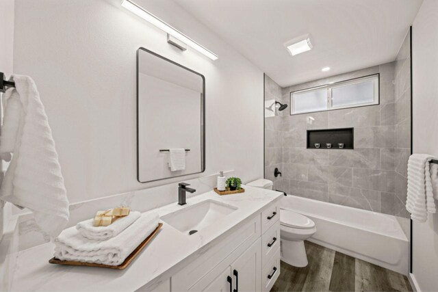 full bathroom featuring hardwood / wood-style floors, vanity, toilet, and tiled shower / bath