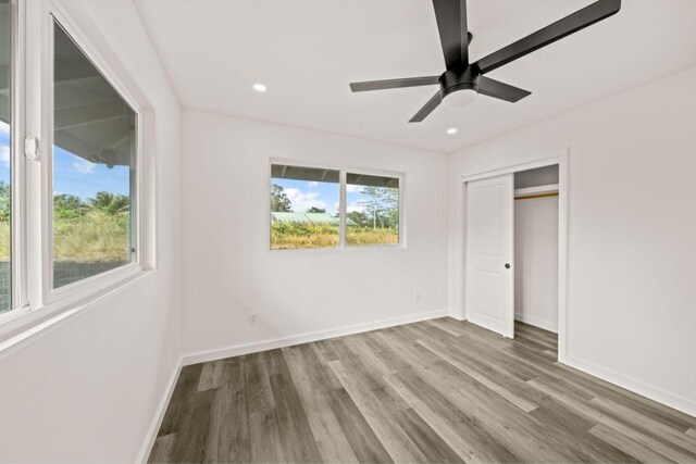 unfurnished bedroom featuring multiple windows, wood-type flooring, a closet, and ceiling fan