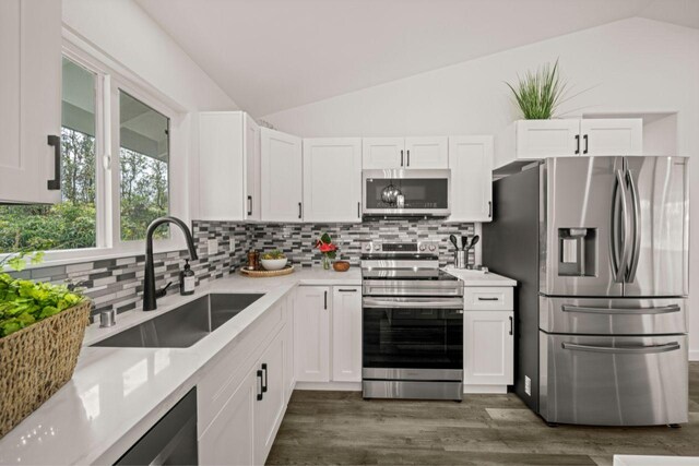 kitchen featuring appliances with stainless steel finishes, tasteful backsplash, sink, white cabinetry, and lofted ceiling