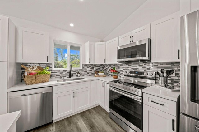 kitchen with white cabinets, appliances with stainless steel finishes, vaulted ceiling, and sink