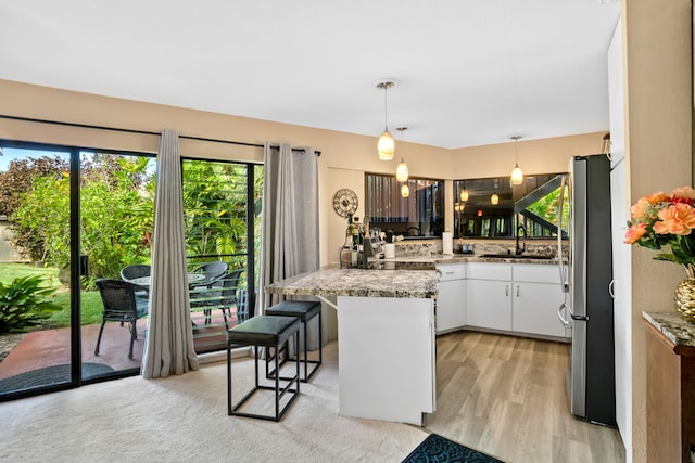 kitchen with kitchen peninsula, a kitchen breakfast bar, light hardwood / wood-style flooring, white cabinets, and hanging light fixtures