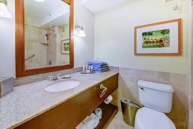 bathroom with a tile shower, vanity, tile walls, and toilet