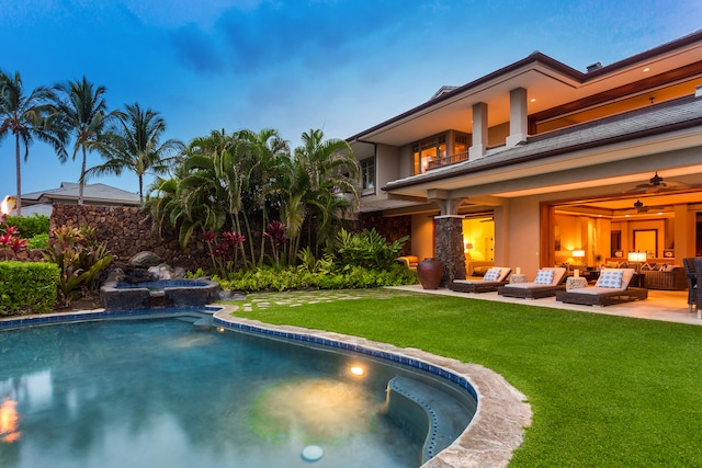 pool at dusk featuring a yard, an outdoor living space, ceiling fan, and a patio area