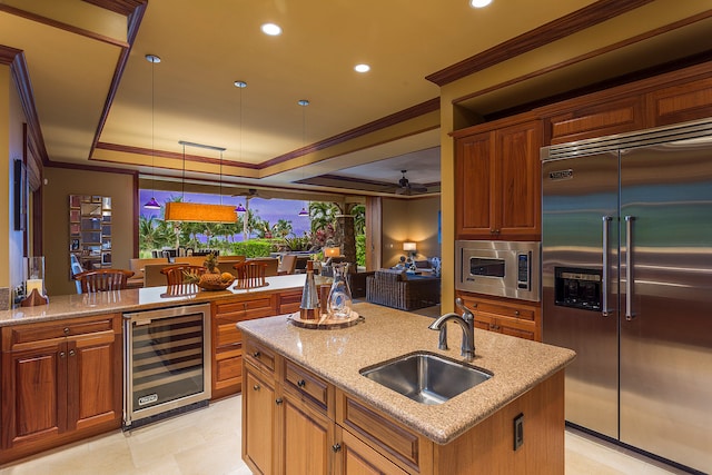 kitchen featuring sink, pendant lighting, built in appliances, a center island with sink, and wine cooler