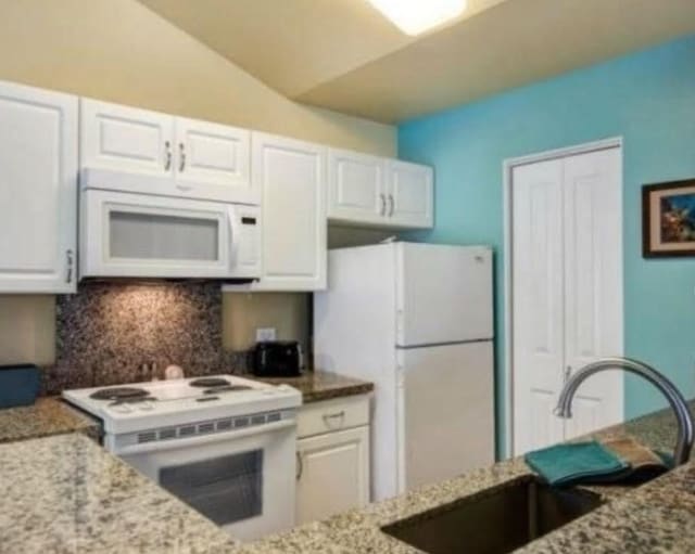 kitchen with lofted ceiling, white cabinetry, sink, and white appliances