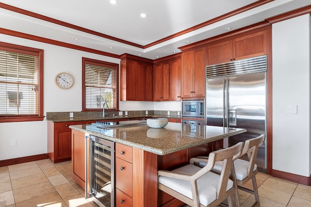 kitchen featuring a center island, a kitchen bar, built in appliances, dark stone counters, and beverage cooler