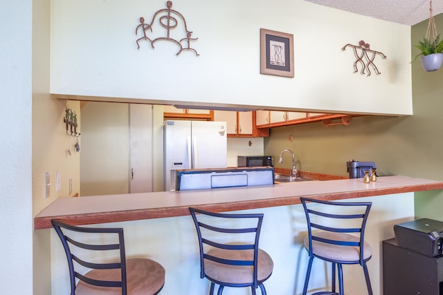 kitchen with white fridge with ice dispenser, sink, kitchen peninsula, a textured ceiling, and a breakfast bar area