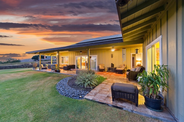 back house at dusk with outdoor lounge area, solar panels, a patio area, and a lawn