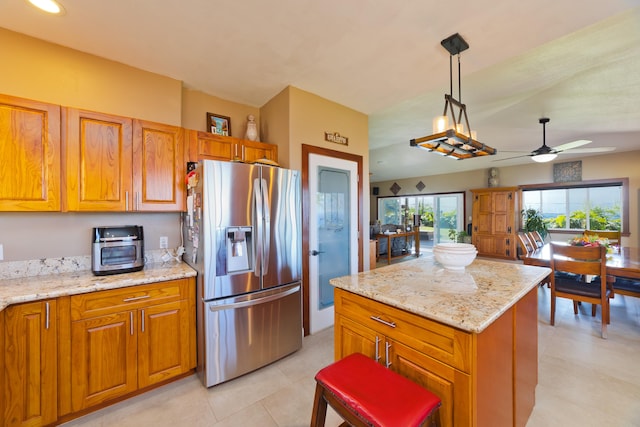 kitchen featuring stainless steel refrigerator with ice dispenser, ceiling fan, light stone countertops, decorative light fixtures, and a kitchen island