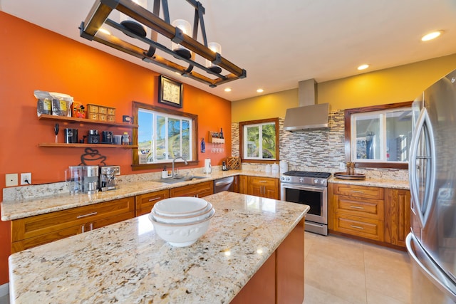 kitchen with decorative backsplash, light stone counters, stainless steel appliances, sink, and wall chimney range hood