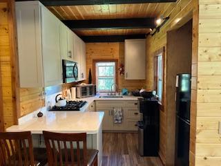 kitchen with white cabinets, sink, beamed ceiling, and wood walls